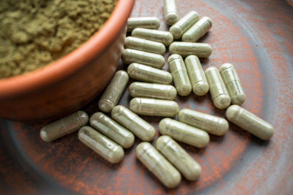 Green kratom powder and capsules on a terracotta colored surface