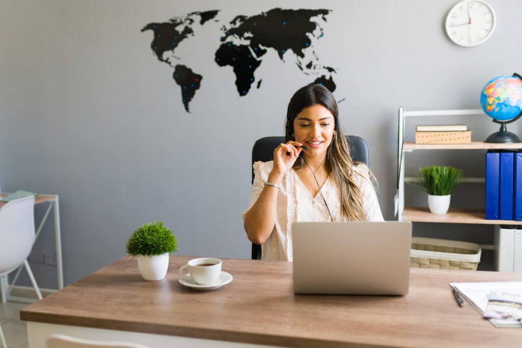 Travel agent taking a phone call at her desk while enjoying coffee and working on her laptop