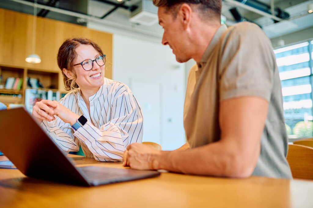 Woman and man in smart casual attire smiling and discussing a laptop at a modern office table