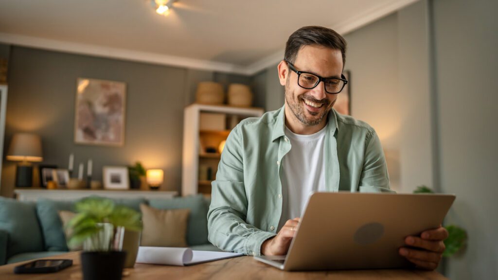 Man sitting at a table working on his laptop and smiling